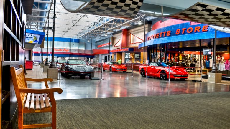 An indoor showroom displays red sports cars, next to a store labeled 