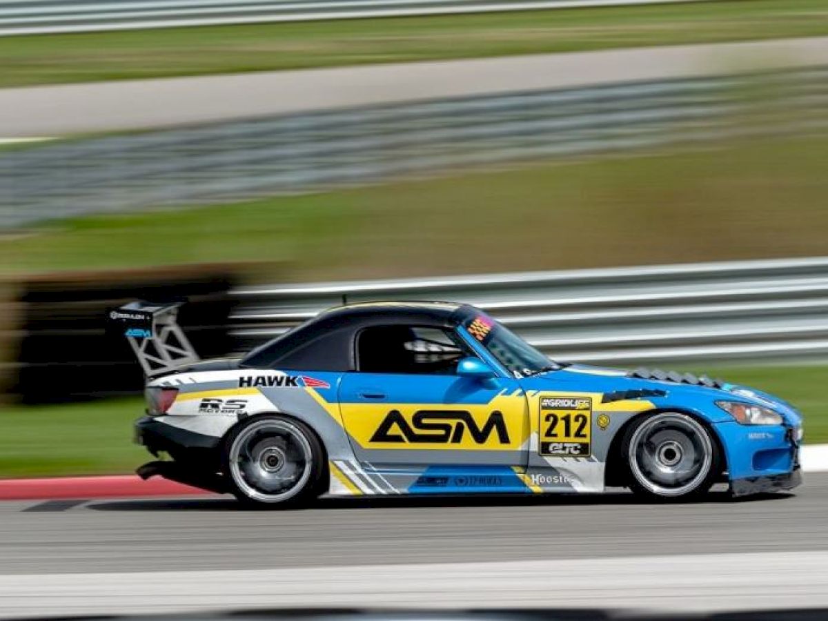 A blue and yellow race car with "ASM" and number "212" speeds on a track, with blurred background suggesting motion.