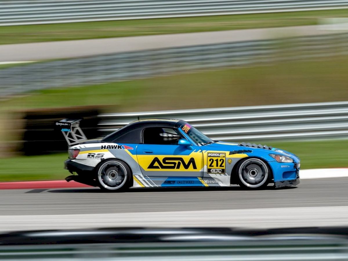 A blue and yellow race car with the number 212 on the side driving on a race track, blurred background indicating high speed.