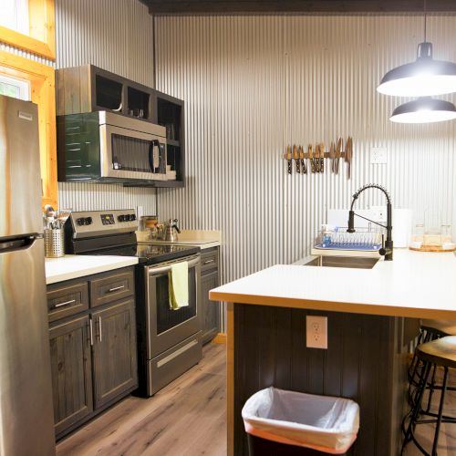 A modern kitchen with stainless steel appliances, an island with stools, wooden cabinets, and a window with a scenic view outside.