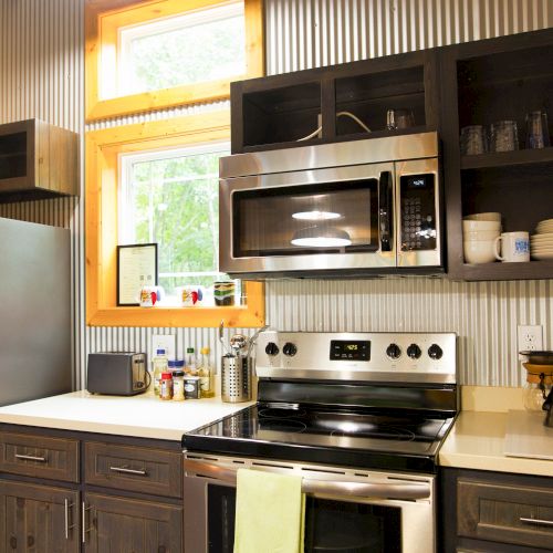 A modern kitchen with stainless steel appliances, dark wood cabinets, a window, and various kitchen items on the counter and shelves.