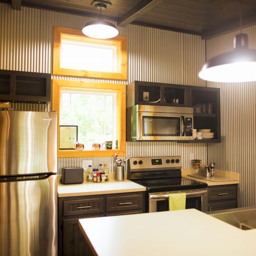 A modern kitchen with metal accents, featuring a refrigerator, stove, microwave, and sink. Bright lights illuminate the space.