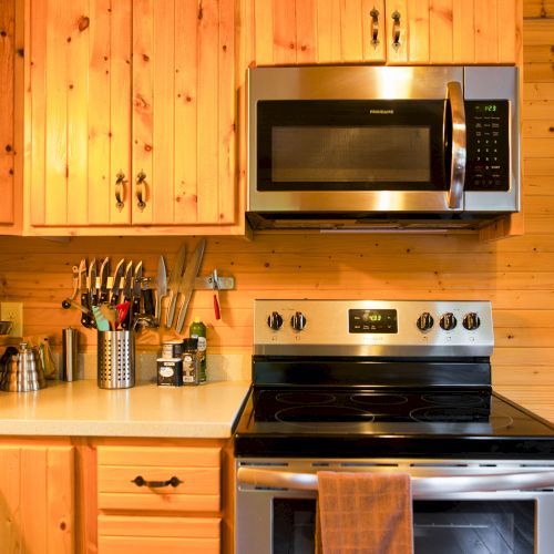 A modern kitchen with wood cabinets, stainless steel appliances, utensils, and a towel hanging on the oven door.