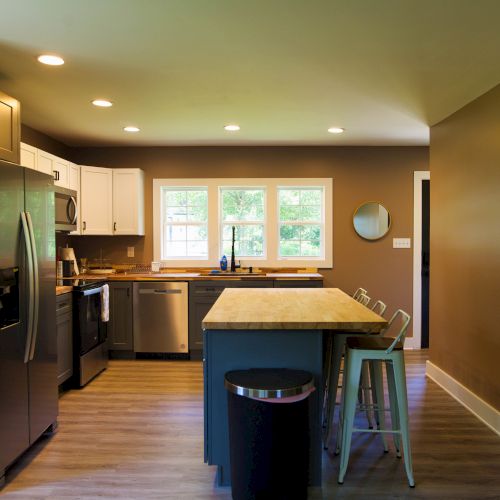 This image shows a modern kitchen with stainless steel appliances, wooden countertops, an island with bar stools, and ample natural lighting.