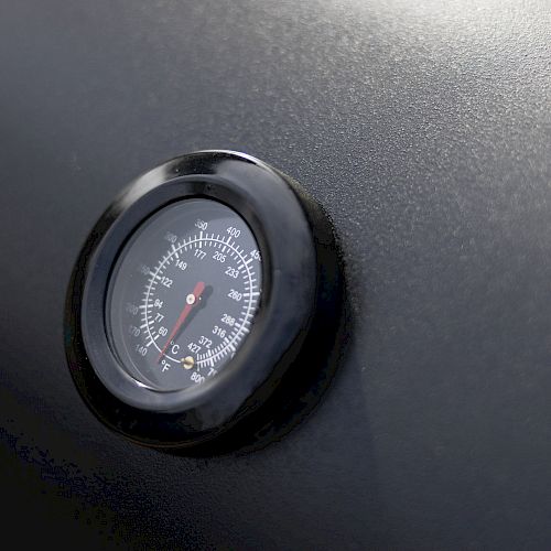 The image shows a close-up of a round gauge with measurement markings, probably for temperature or pressure, mounted on a black surface.