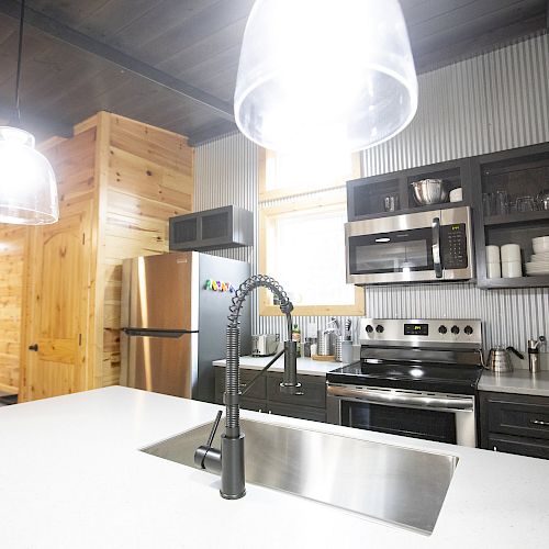 A modern kitchen with a stainless steel sink, appliances, a white countertop, black cabinets, and pendant lights hanging from the ceiling.