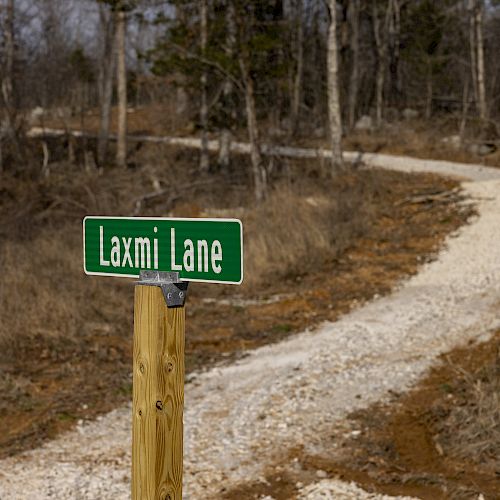 A rural, unpaved winding path in a forested area with a green street sign reading 