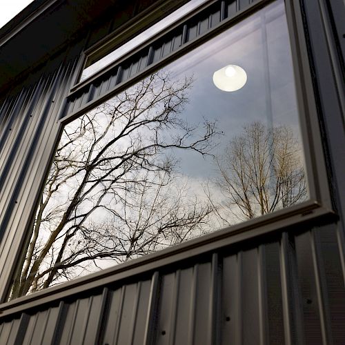 A reflective window on a metal building with the image of trees and the sky mirrored in it.