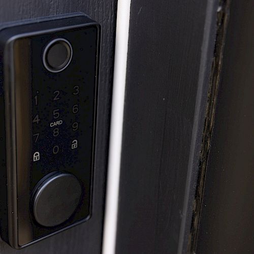 The image shows an electronic door lock with a keypad and a card reader on a black door, featuring a circular knob at the bottom.