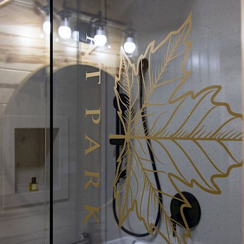 A bathroom with glass shower doors featuring a large golden leaf design. Inside the shower is a built-in shelf with a small yellow bottle.