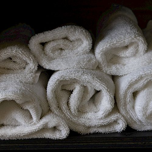 Five neatly rolled white towels are stacked in two rows inside a dark storage shelf.