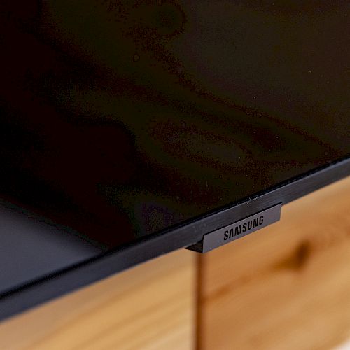 This image shows a close-up of the lower corner of a Samsung television screen resting on a wooden surface.