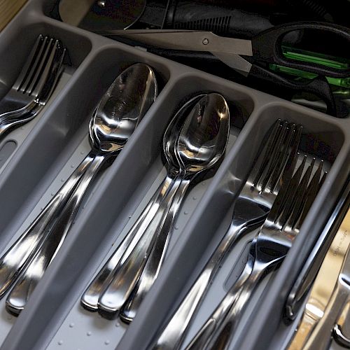 The image shows an open drawer containing organized silverware, including forks, spoons, knives, and a pair of scissors.