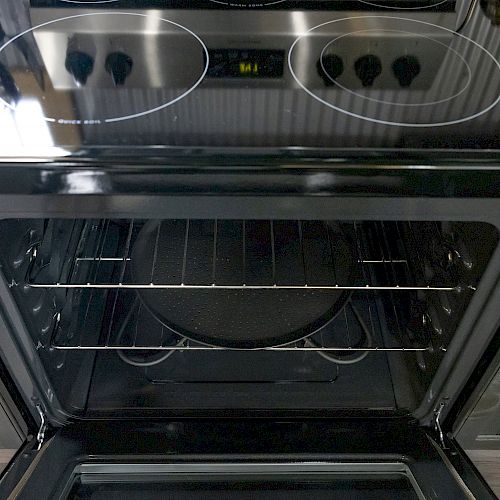 The image shows a kitchen stove with an open oven door, displaying an empty oven with two racks inside. The stove has four electric burners.