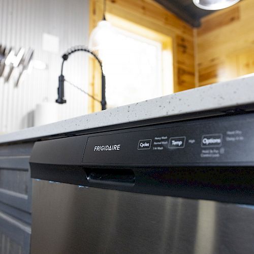 The image shows a modern kitchen with a Frigidaire dishwasher, a countertop, cabinets, and a faucet, with knives in the background.