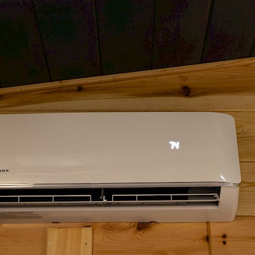 A wall-mounted split air conditioner is installed on a wooden wall, displaying 