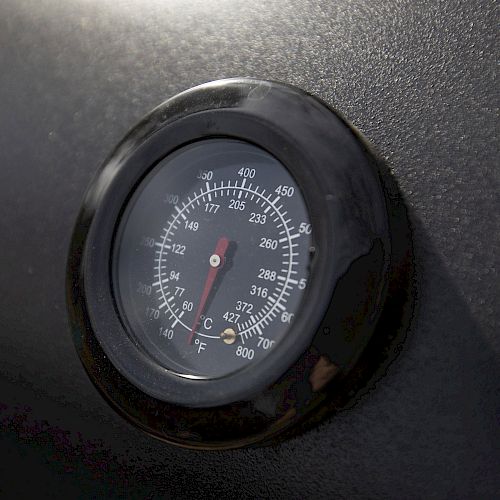 The image shows a close-up of a round analog thermometer mounted on a black surface, displaying temperature readings in both Fahrenheit and Celsius.