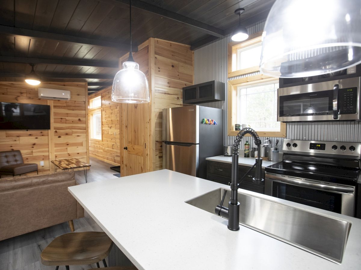 A modern kitchen and living area with wooden walls, a white countertop island, stainless steel appliances, and a cozy sitting space.