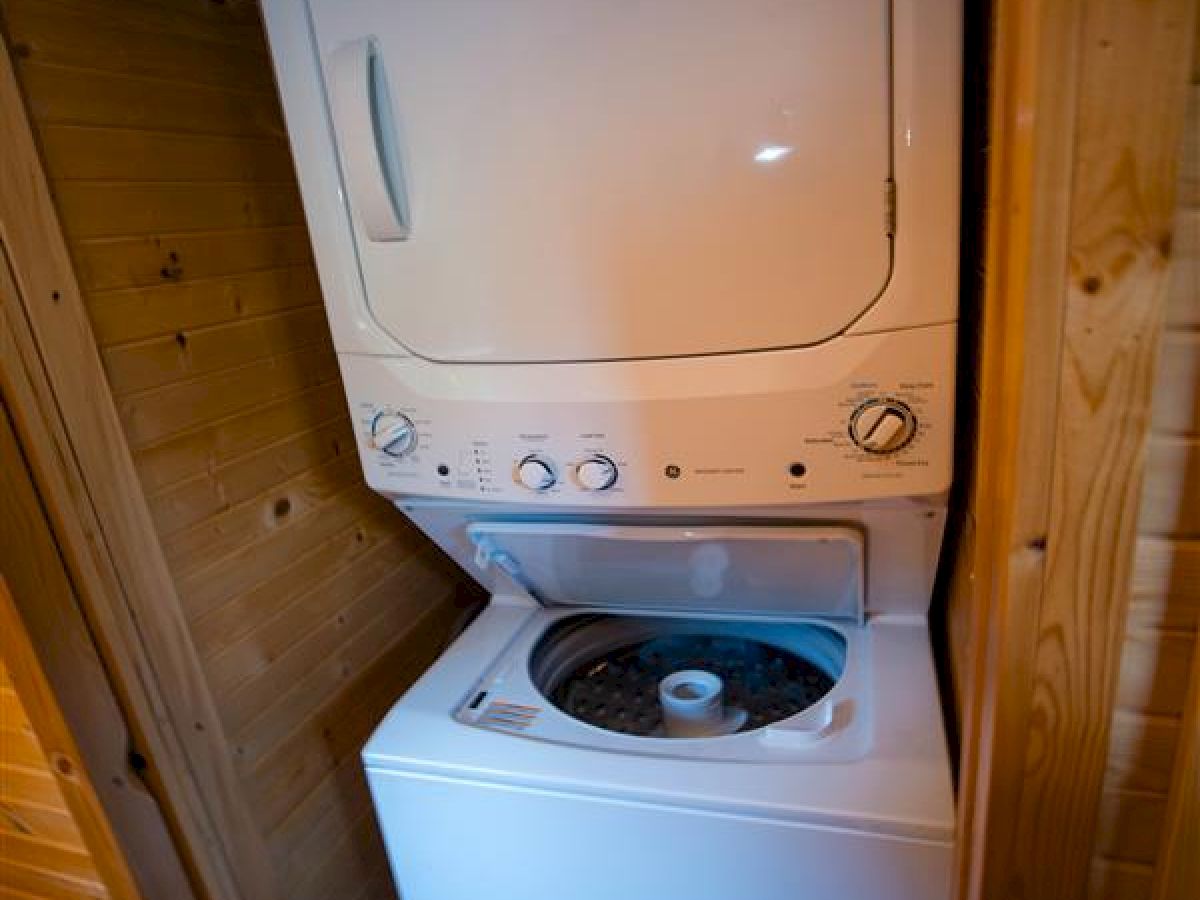 This image shows a stacked washer and dryer unit placed in a wooden enclosure. The top dryer door is closed, while the washer lid is open.