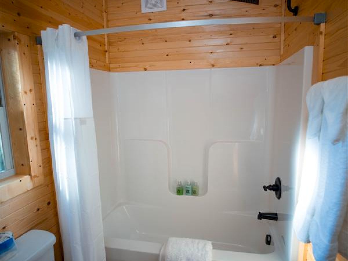 A cozy bathroom with wood-paneled walls, a white bathtub and shower curtain, a toilet, towel rack, and a window casting light.