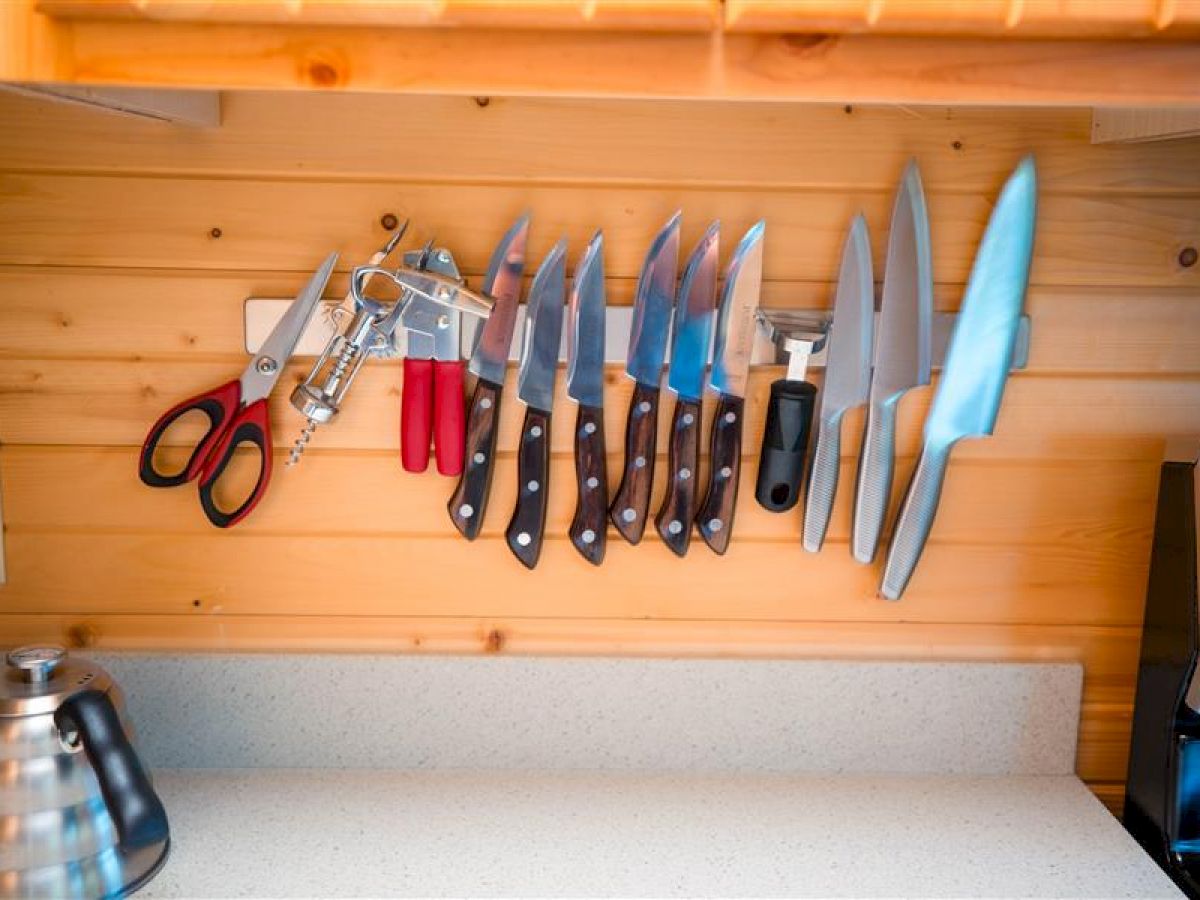 A kitchen area with a magnetic strip holding various knives and kitchen tools on a wooden wall; a kettle is placed on the countertop.