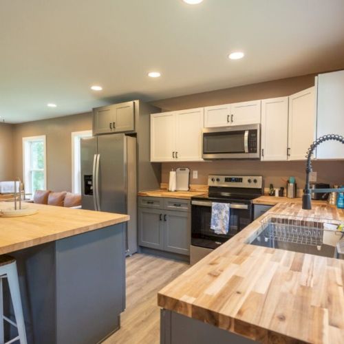 A modern kitchen with wooden countertops, stainless steel appliances, an island with stools, and a large sink facing a window.