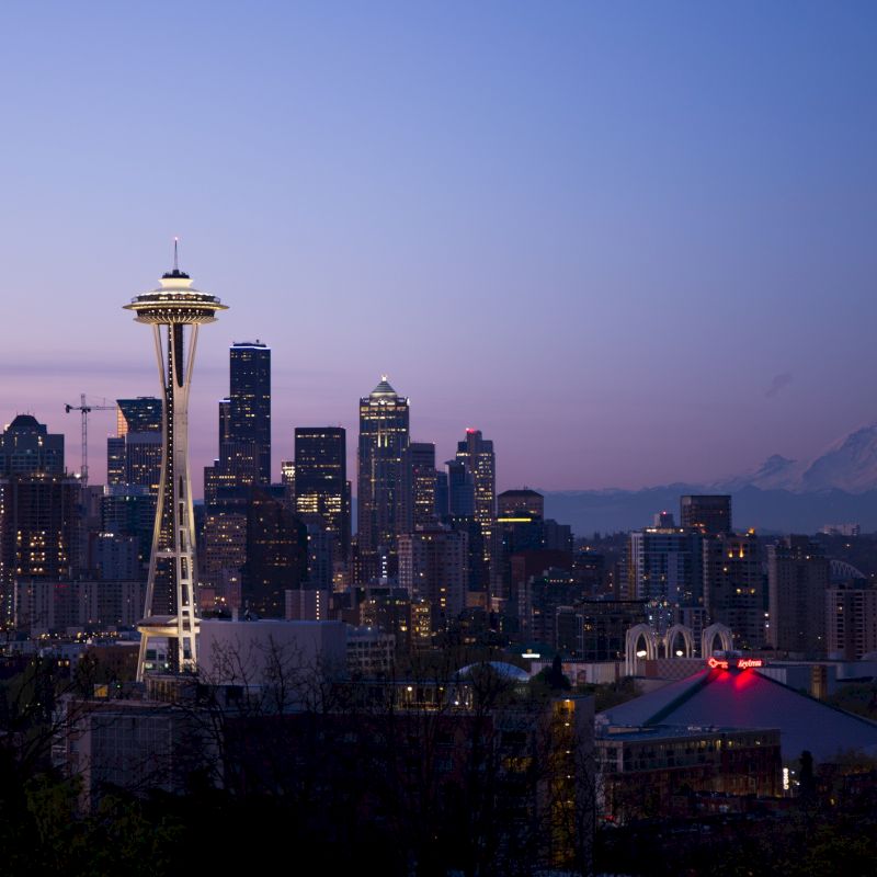 Image shows Seattle's skyline at dusk featuring the Space Needle, surrounding buildings, and Mount Rainier in the background.