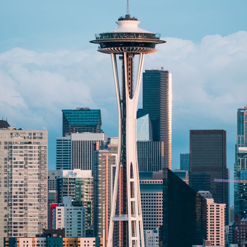 The image shows the Space Needle in Seattle, a prominent observation tower, with the city's skyline in the background under a partly cloudy sky.