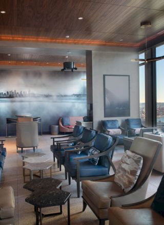 A modern lounge with large windows, comfortable seating, and a scenic view of a Ferris wheel and waterfront in the background, with ambient lighting.