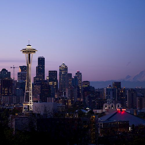The image shows the Seattle skyline at dusk, featuring the Space Needle and city buildings, with Mount Rainier visible in the background.