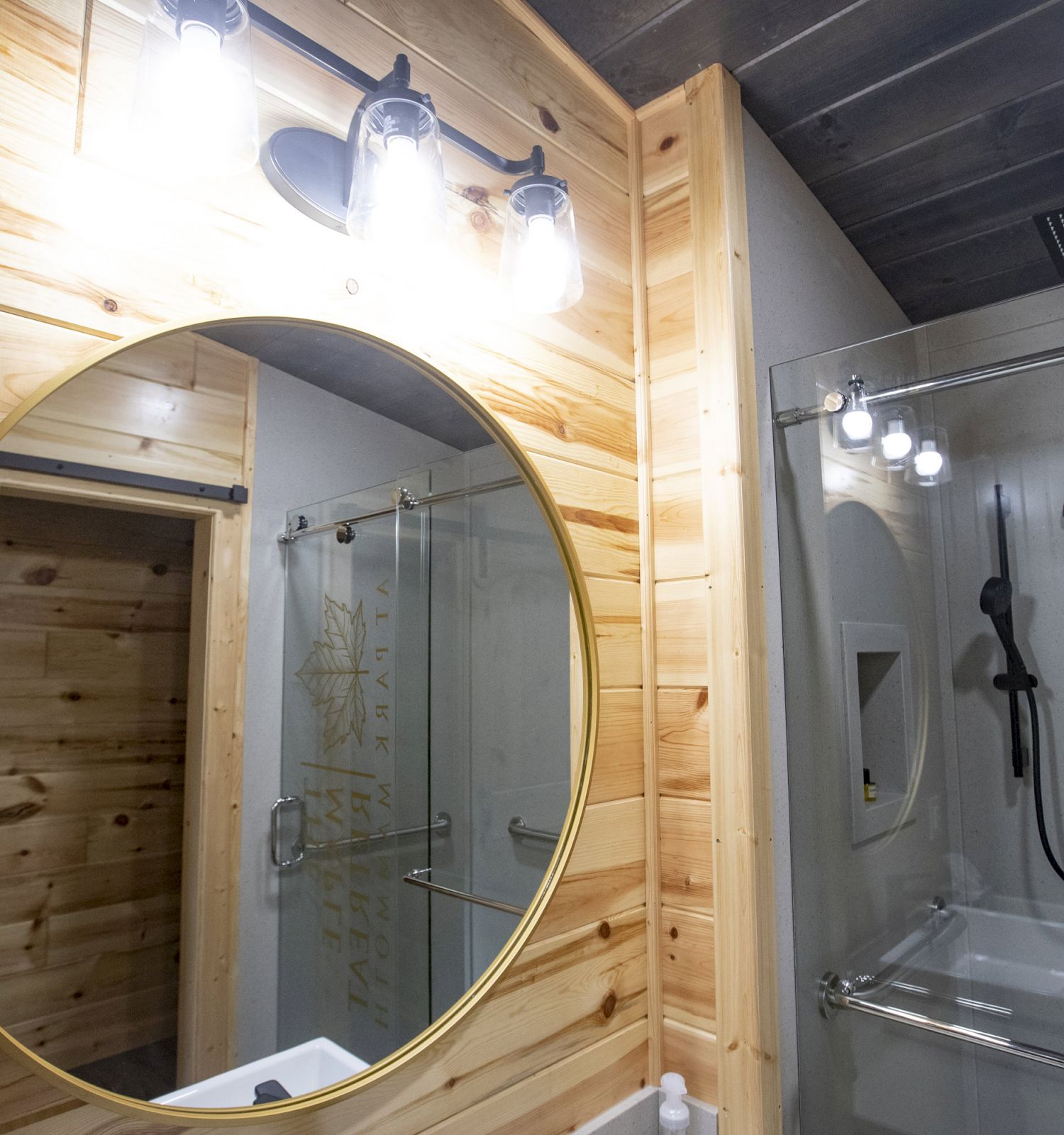 A modern bathroom features a round mirror with wood paneling, a glass-enclosed shower, a black showerhead, and illuminated lighting fixtures.