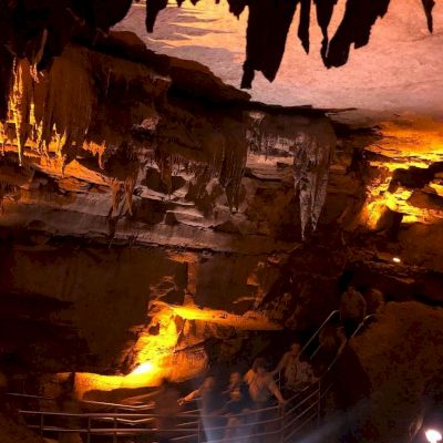 A group of people are exploring an illuminated cave with stalactites hanging from the ceiling and rock formations visible.